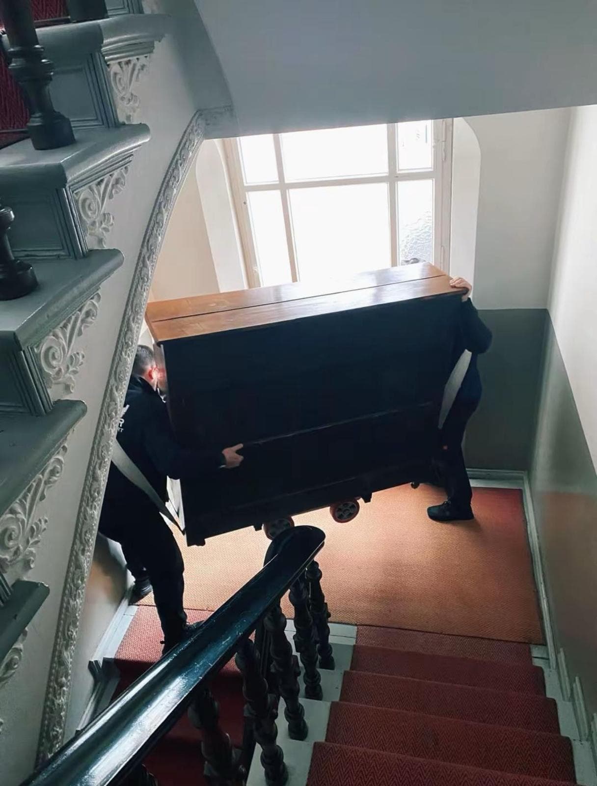 Umzugshelfer transportieren ein Klavier mit Tragegurten eine Treppe hinunter