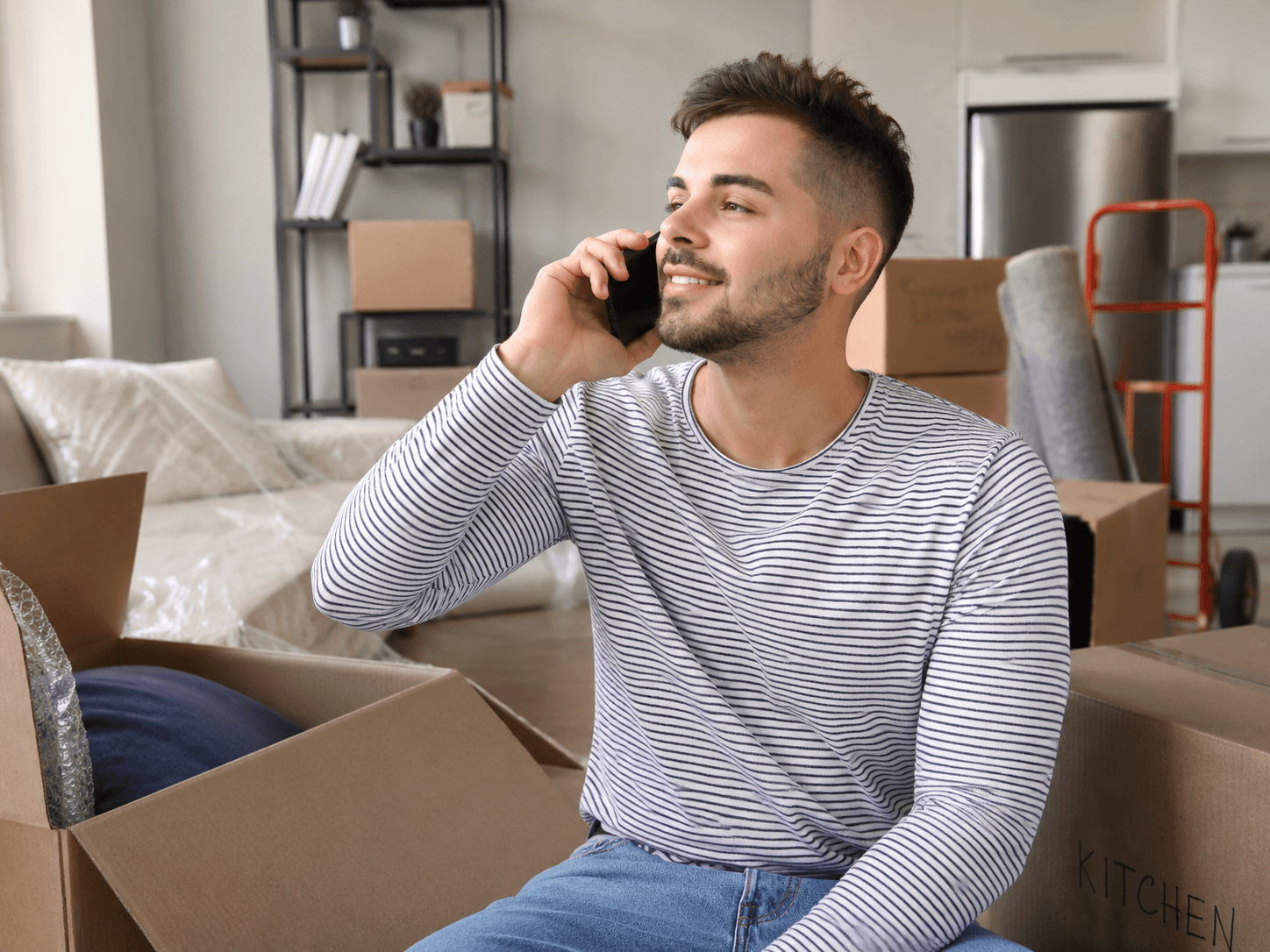 Mann telefoniert entspannt zwischen Umzugskartons